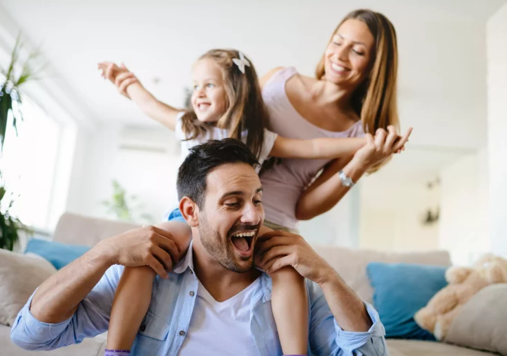 Symbolfoto von 5min.at: Eine glückliche Familie spielt zuhause im Wohnzimmer.