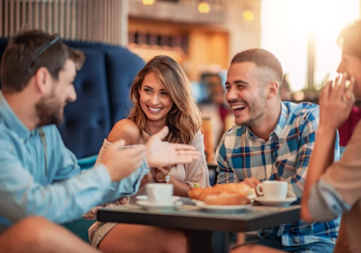 Symbolfoto von 5min.at: Vier Freunde sitzen mit einem Kaffee in einem Restaurant und lachen.