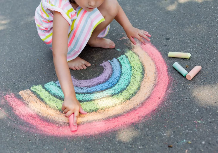 Symbolfoto von 5min.at: Kind malt mit bunter Straßenkreide einen Regenbogen.