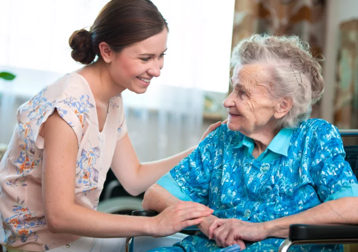 Symbolfoto von 5min.at: Pflegerin kümmert sich rührend um eine Seniorin im Rollstuhl.