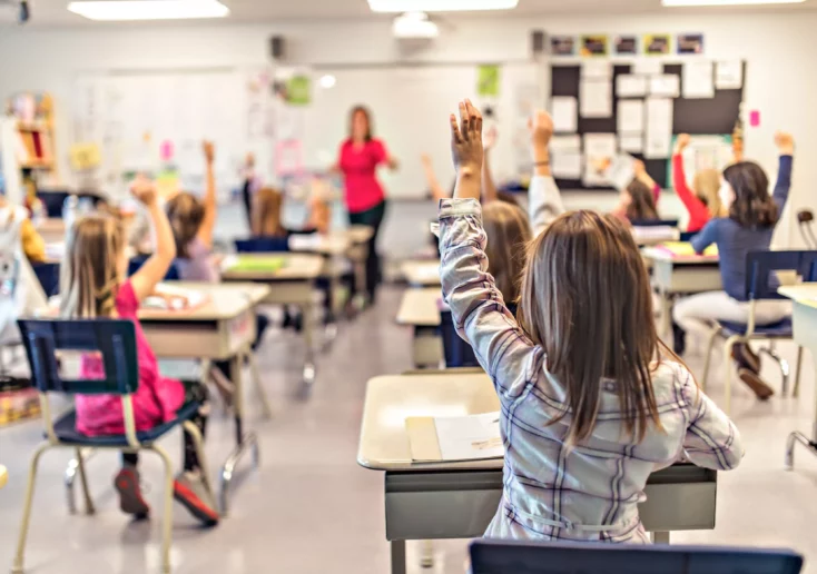 Symbolfoto von 5min.at: Schulkinder sitzen im Klassenzimmer und zeigen auf.