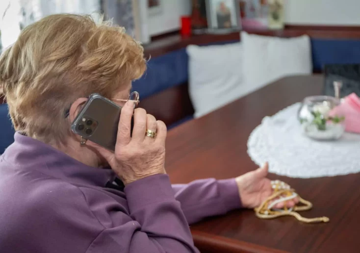 Symbolfoto zu einem Beitrag von 5min.at: Eine ältere Dame sitzt an einem Tisch und telefoniert.