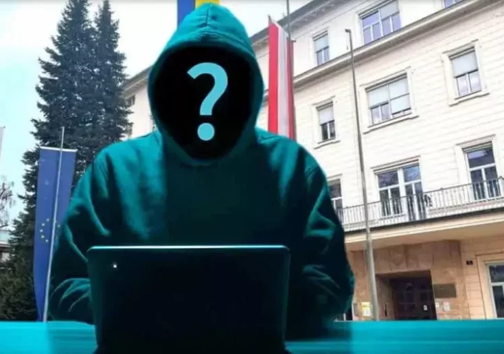 Symbolfoto zu einem Beitrag von 5min.at: Ein unbekannter Hacker sitzt vor einem öffentlichen Gebäude und arbeitet an seinem Laptop