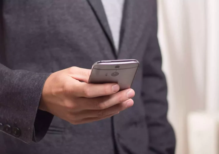 Symbolfoto zu einem Beitrag von 5min.at: Ein Mann im Anzug hält ein Handy in der Hand