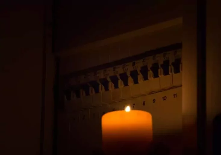 Symbolfoto zu einem Beitrag von 5min.at: Eine Kerze steht vor einem Zählerkasten