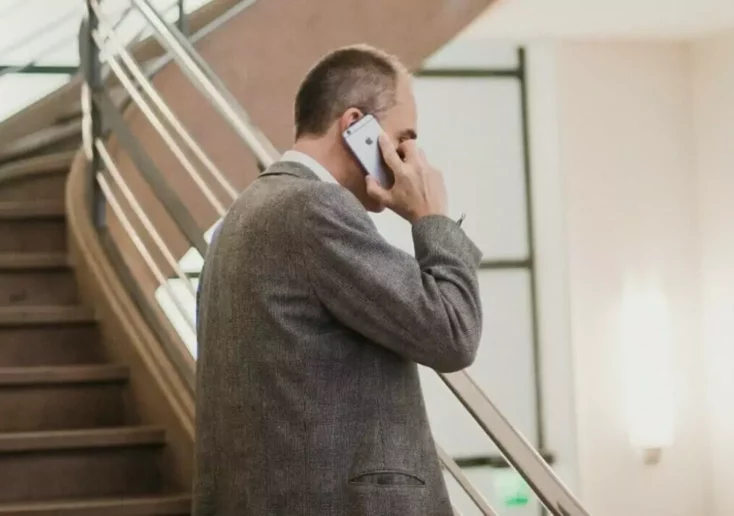 Symbolfoto zu einem Beitrag von 5min.at: Ein Mann im Anzug steht vor einer Treppe und telefoniert