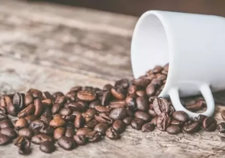 Symbolfoto von 5min.at: Leere Kaffeetasse mit ausgeschütteten Kaffebohnen liegt auf einem Tisch.
