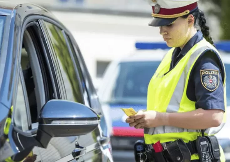 Symbolfoto von 5min.at: Polizistin kontrolliert die Fahrzeugpapiere.