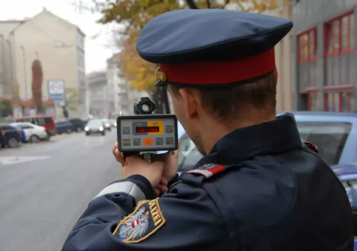 Symbolfoto von 5min.at: Polizist misst die Fahrgeschwindigkeit mittels Messpistole.