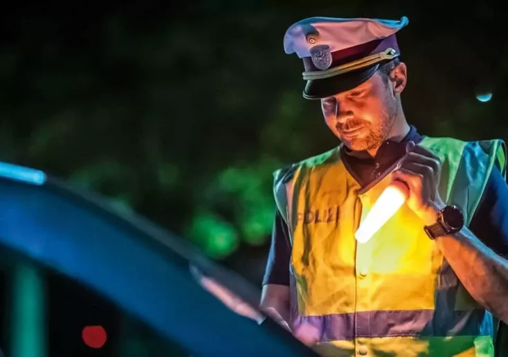 Symbolfoto zu einem Beitrag von 5min.at: Ein Polizist kontrolliert ein Auto bei Nacht
