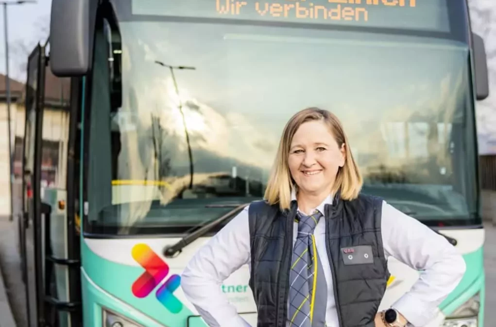 Foto auf 5min.at zeigt eine Busfahrerin, welche glücklich vor einem Bus der Kärntner Linien steht.
