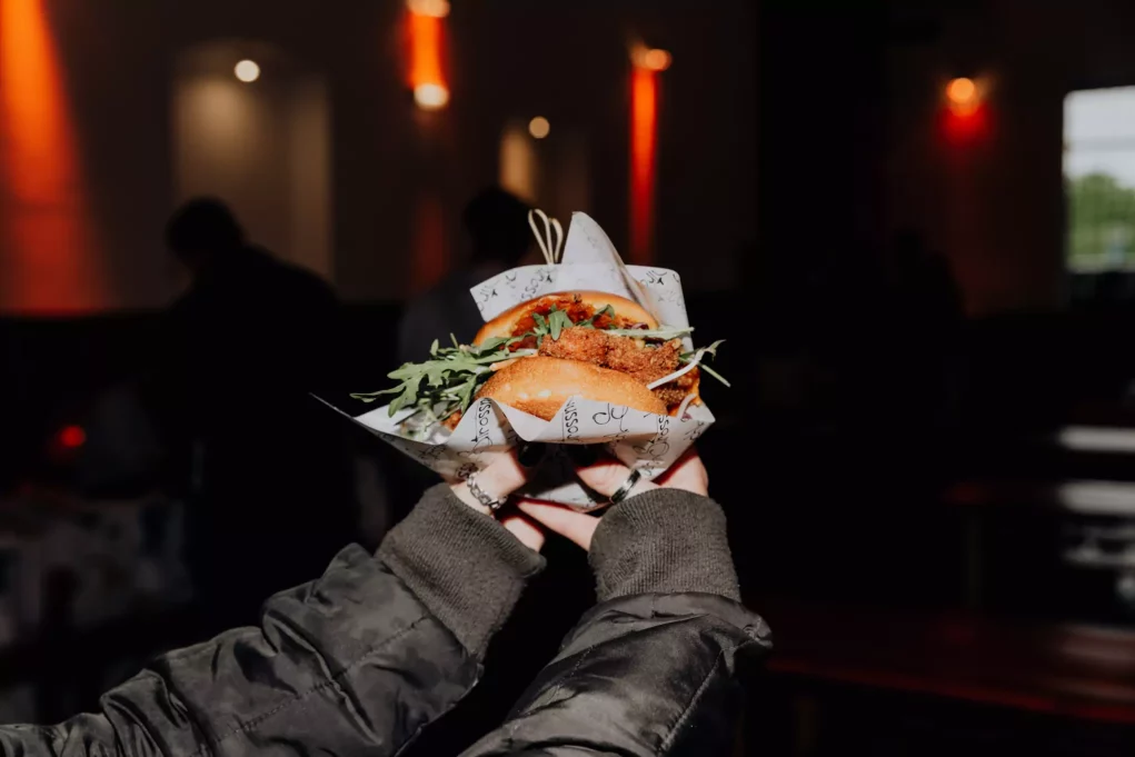 Foto auf 5min.at zeigt einen knusprig leckeren Burger, der von einer Person in den Händen gehalten wird.