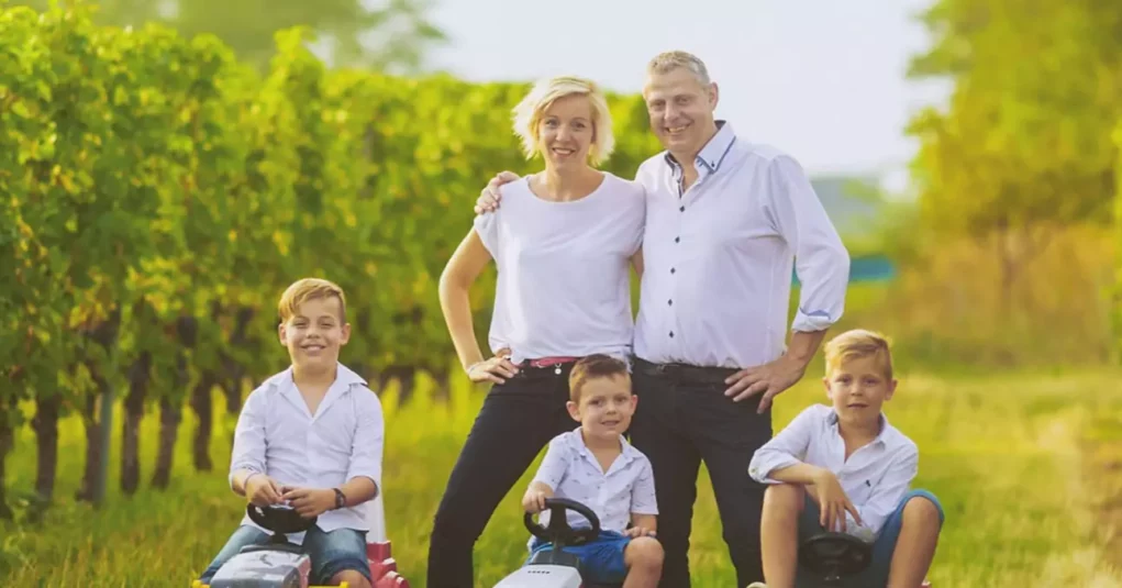 Foto im Beitrag von 5min.at: Glückliche Familie mit drei Kindern steht auf einem Weingut.