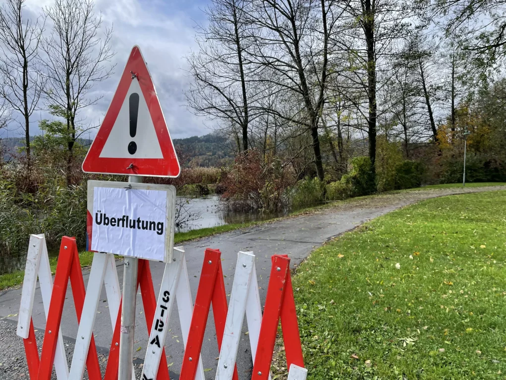 Bild auf 5min.at zeigt einen über die Ufer getretenen Fluss, samt Schild mit Aufschrift "Überflutung".