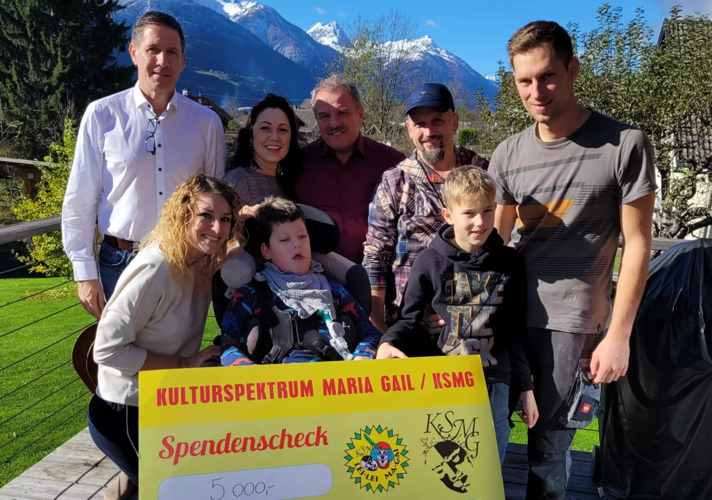 Ein Bild auf 5min.at zeigt Vertreter des Vereins "Kulturspektrum Maria Gail" mit dem kleinen Marius, der im Rollstuhl sitzt, und seiner Familie bei der symbolischen Scheckübergabe.
