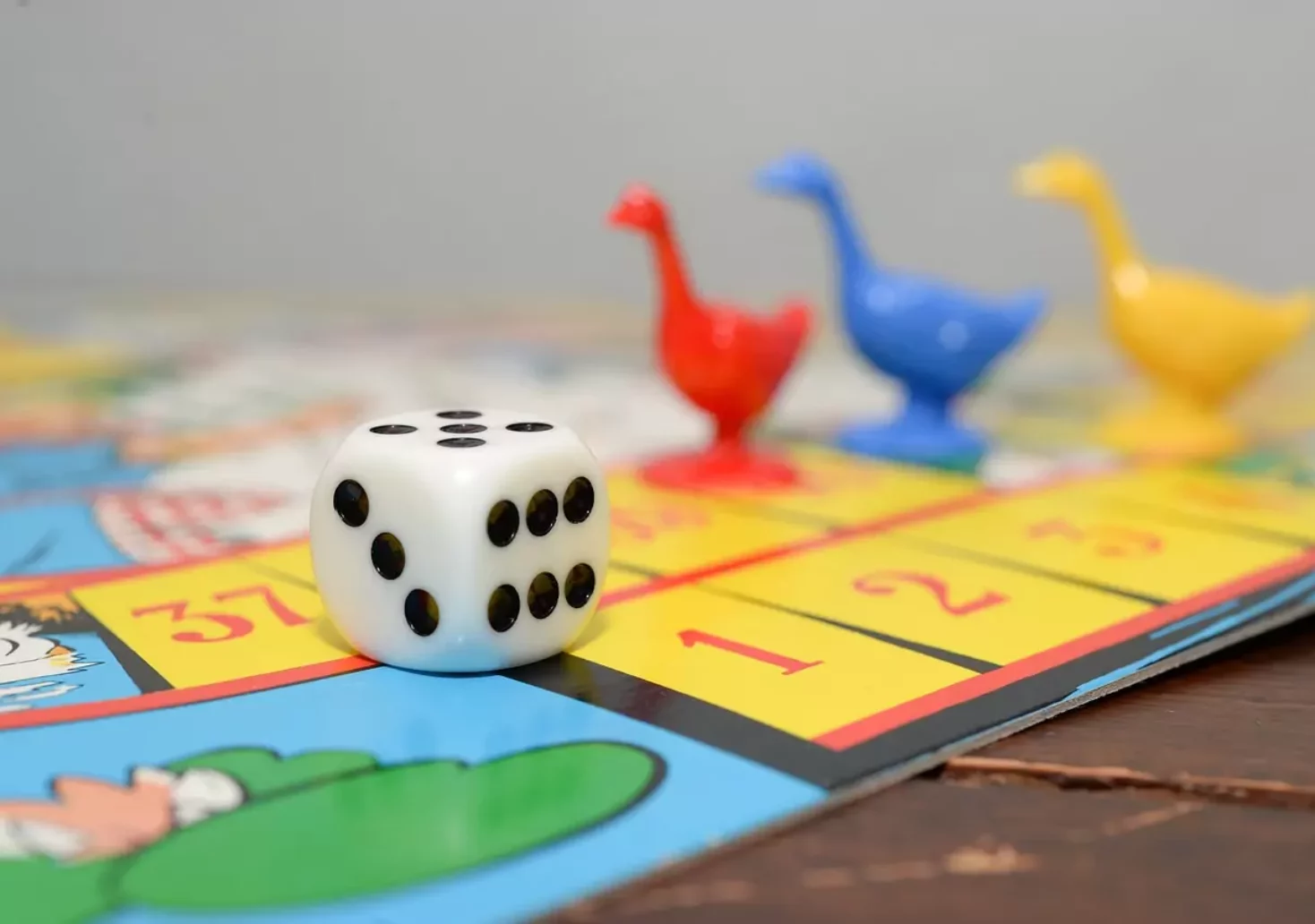 Ein Bild auf 5min.at zeigt ein Brettspiel. Die Spielfiguren bestehen aus bunten Gänsen und ein Würfel liegt am Spielbrett.