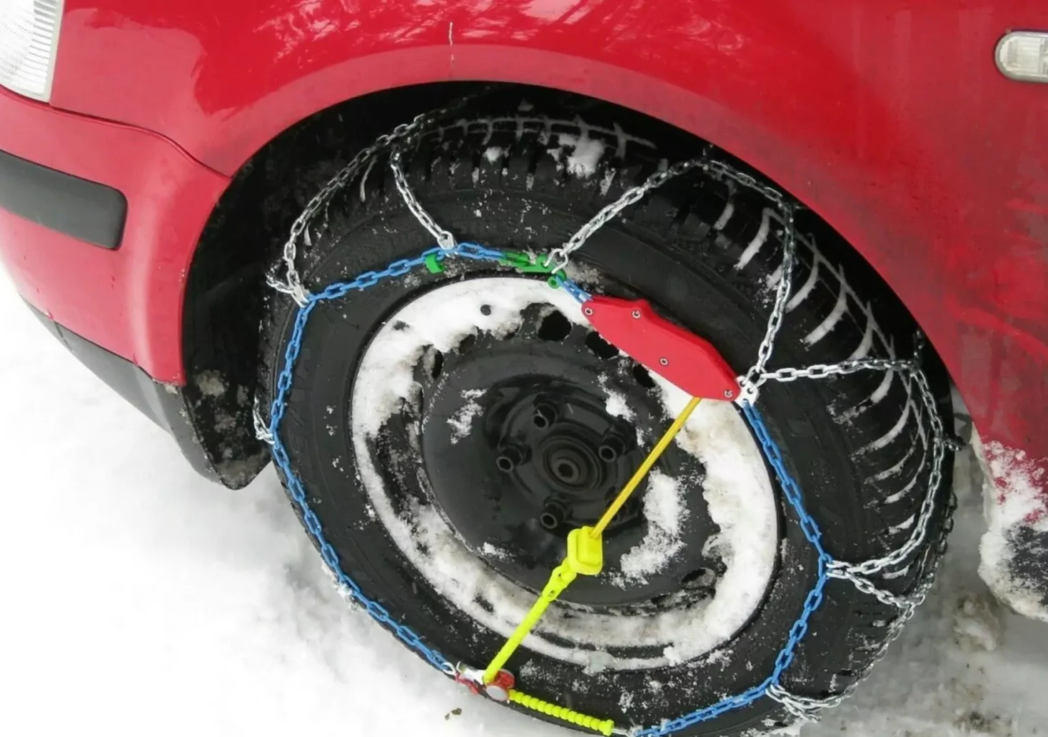 Ein Bild auf 5min.at zeigt ein rotes Auto auf dessen Reifen Schneeketten montiert wurden.