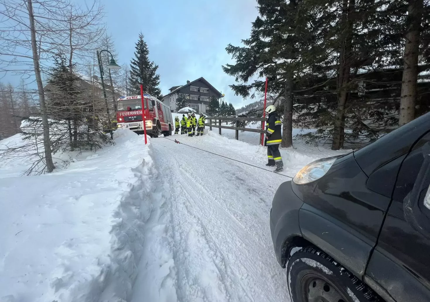 Foto in Beitrag von 5min.at: Zu sehen ist ein Feuerwehrauto und einige Feuerwehrmänner, die einen Lieferwagen, der auf der Schneefahrbahn nicht mehr weitergekommen ist, abschleppen.