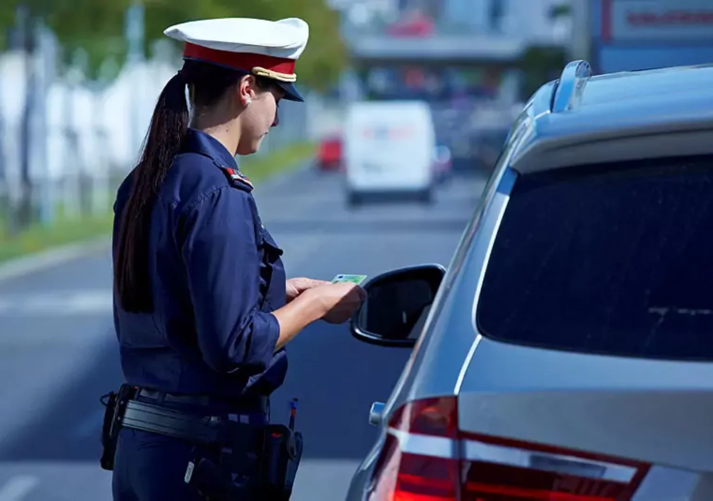 A photo on the 5min.at website shows a policewoman during a traffic stop.  She holds the driver's license in her hands.  There is a car in front of her.