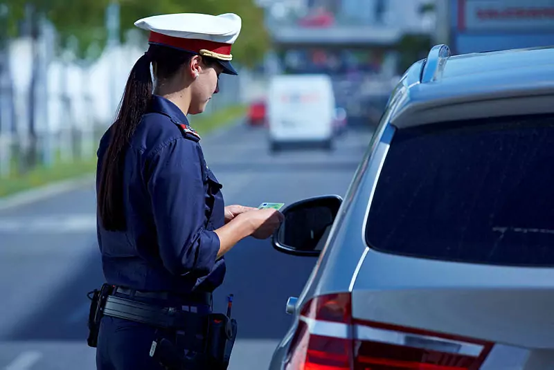 Ein Bild auf 5min.at zeigt eine Polizistin bei einer Verkehrskontrolle. Sie hält einen Führerschein in den Händen. Vor ihr steht ein Auto.