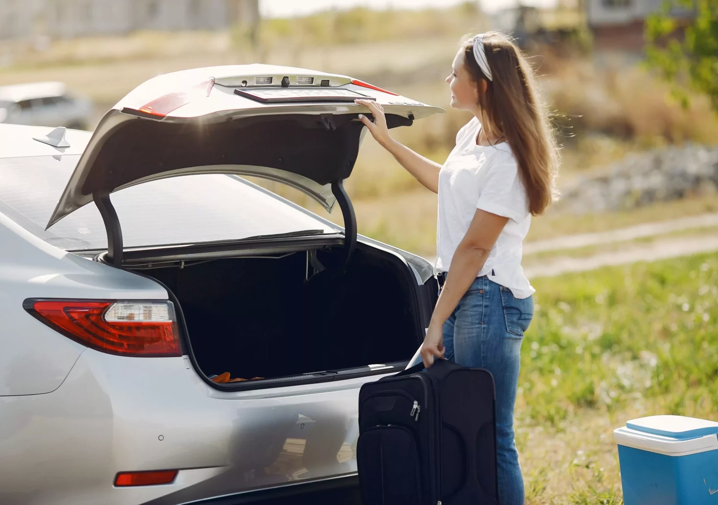 Ein Bild auf 5min.at zeigt eine Frau, die einen Koffer in den Kofferraum eines silbernen Autos lädt.