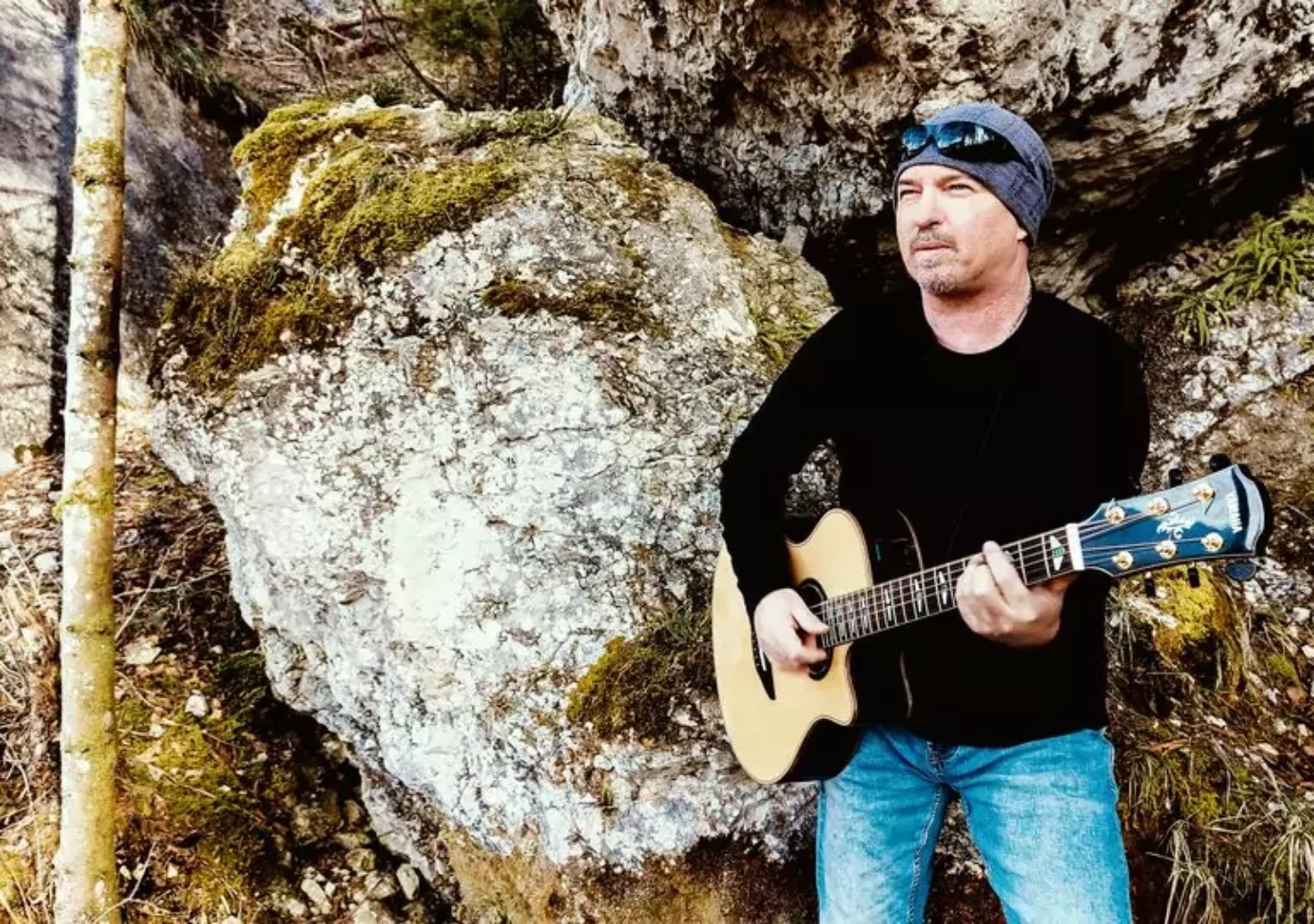 Ein Bild auf 5min.at zeigt den Villacher Songwriter Wolfgang Fischer mit einer Gitarre vor einer Felswand.