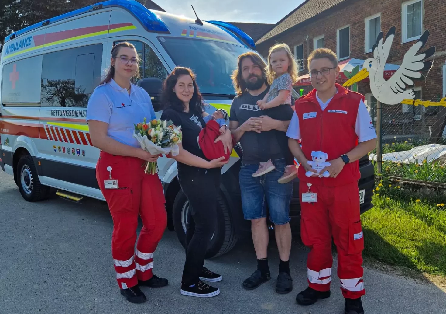 Foto in Beitrag von 5min.at: Zu sehen ist ein Rettungswagen und einige Menschen, die davor stehen, darunter die Familie des Neugeborenen und die Personen vom Roten Kreuz.
