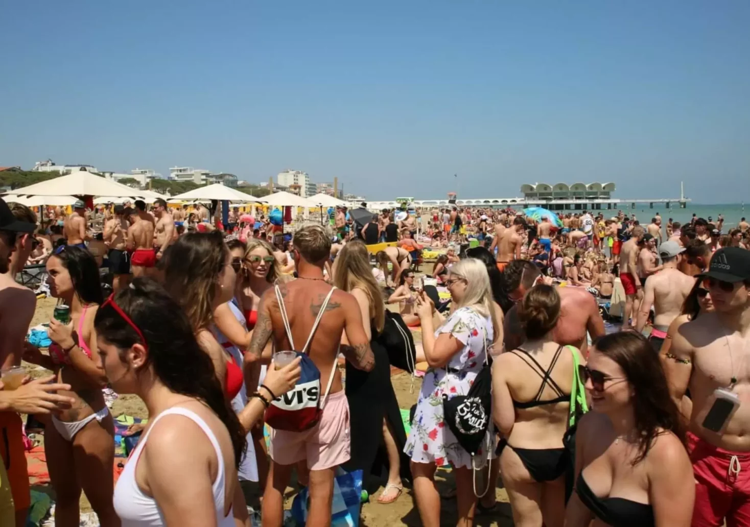 Ein Bild auf 5min.at zeigt Männer und Frauen in Badehosen und Bikinis am Strand von Lignano.