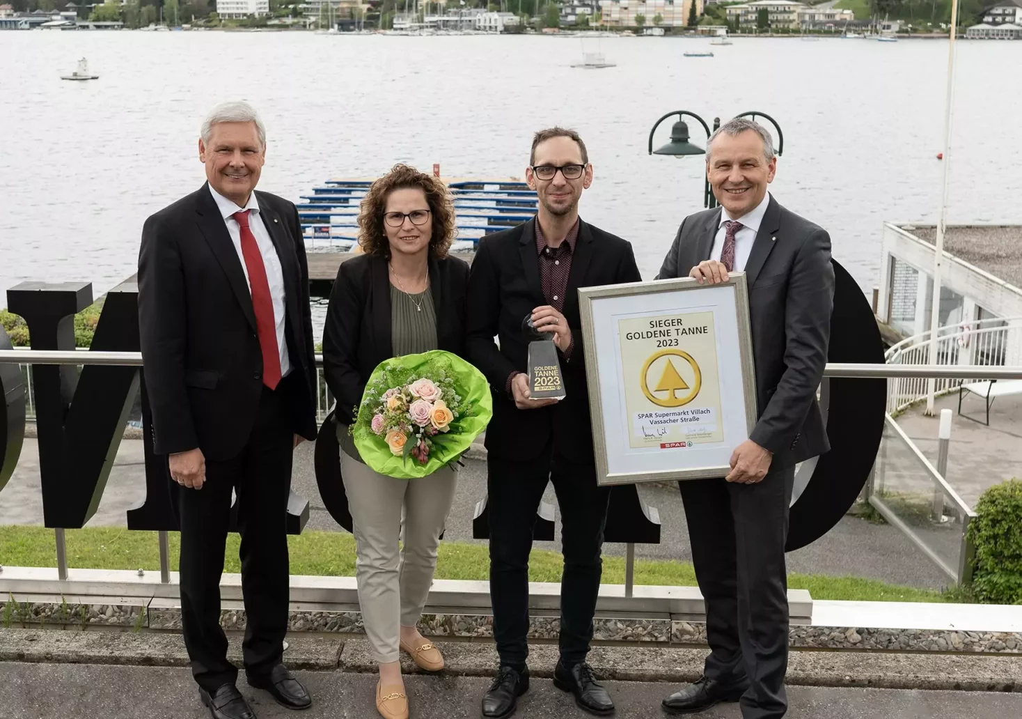 Ein Bild auf 5min.at zeigt Hans K. Reisch, Birgit Dörfler, Thomas Scheiber und Paul Bacher mit der Auszeichnung und einem Blumenstrauß in den Händen.